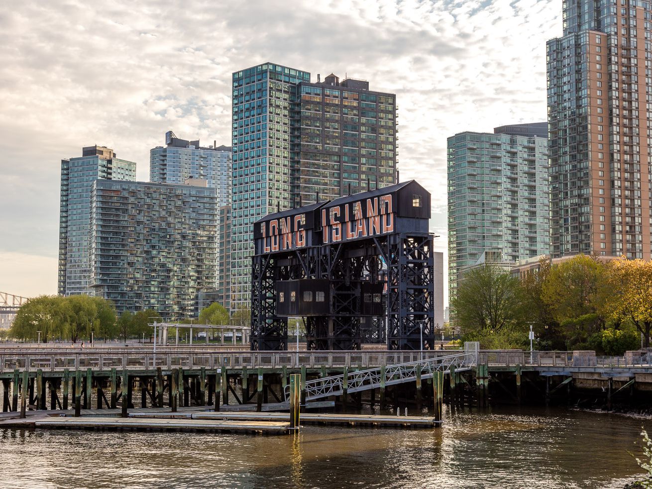 The waterfront in Long Island City. There is a pier with a sign that reads: Long Island. Behind the sign are many tall apartment buildings.