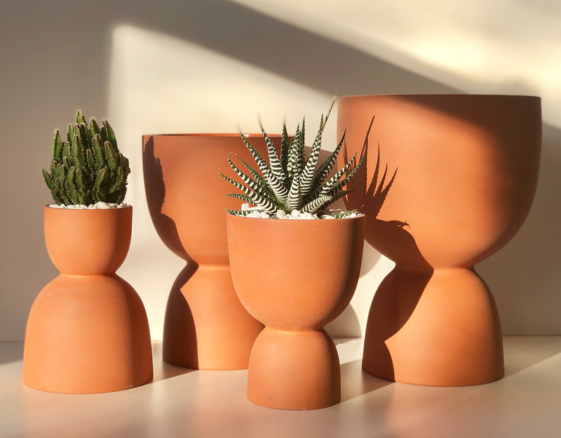Multiple terracotta stacked planters sit on a glossy tan surface. There are various assorted succulents in each planter.