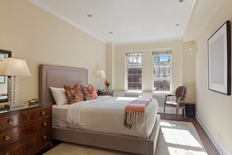 A bedroom with beige walls, a medium-sized bed, and large windows.