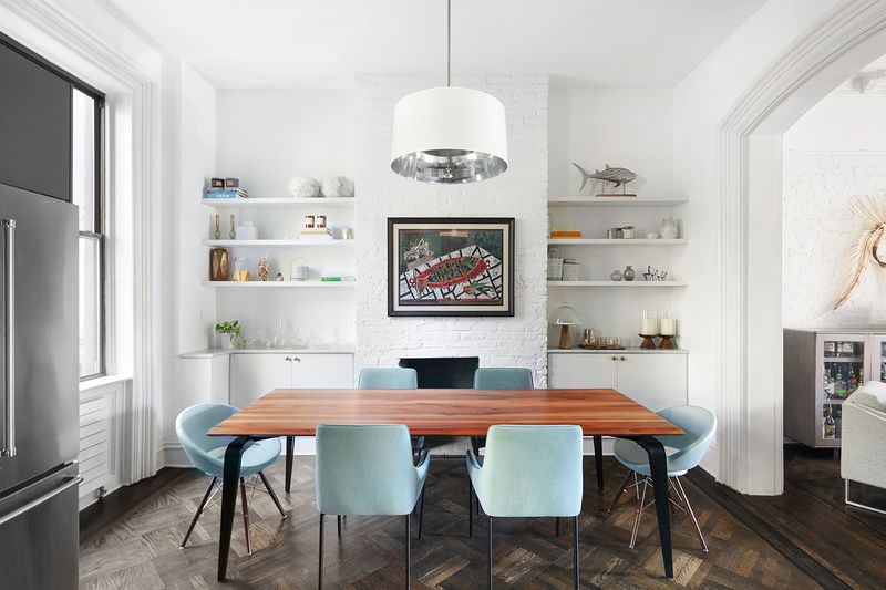 A dining area with a wood dining table, light blue chairs, exposed brick, and hardwood floors.