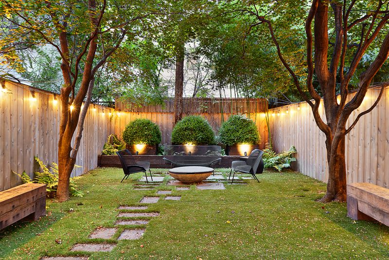 A landscaped garden with two trees, a wooden fence, and a seating area.