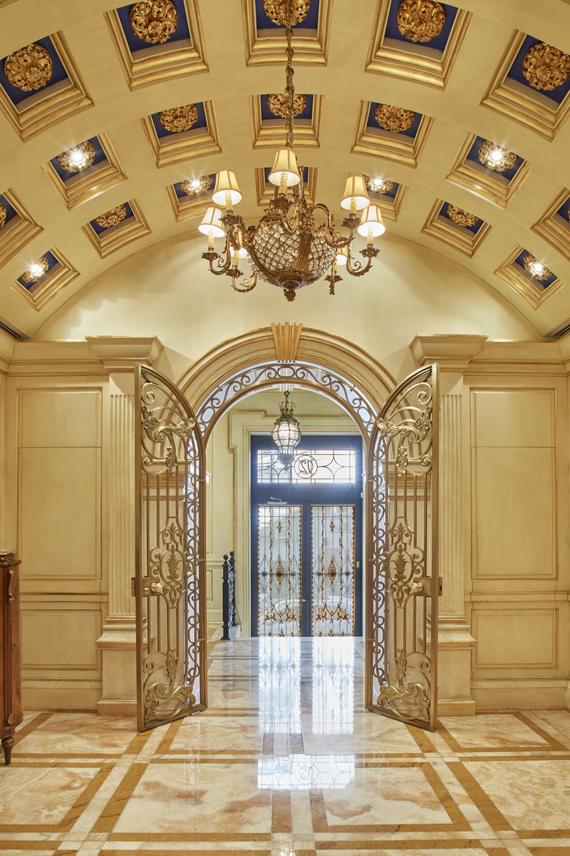 An arched entrance with golden doors, marble floors, and a chandelier.