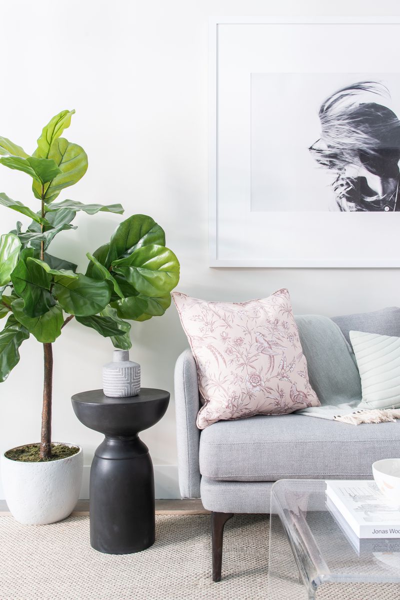 A living room with a grey couch, a planter, and a framed picture hanging on the wall.