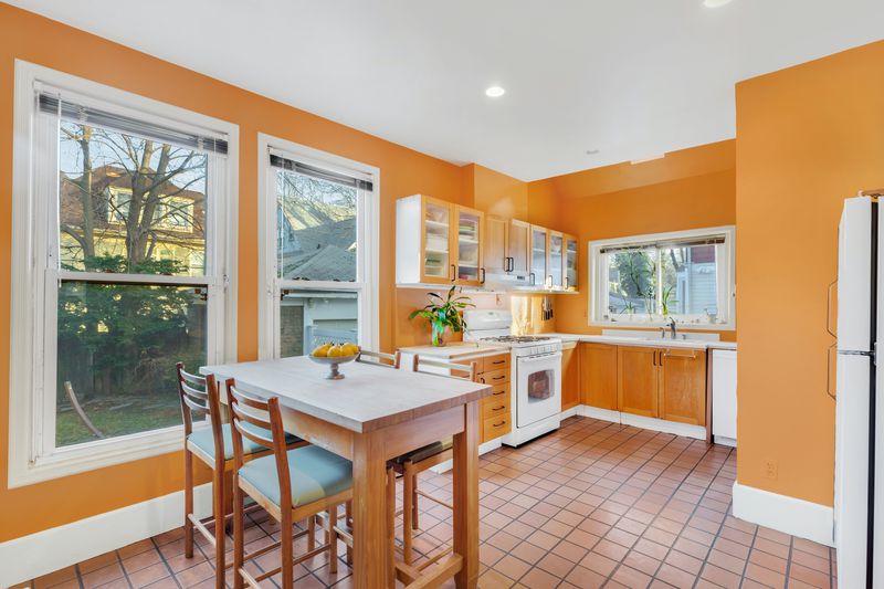 A kitchen with a small table and four chairs, orange walls and cabinets, and three windows. 