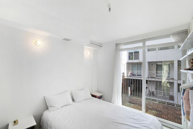 A bedroom with a medium-sized bed, a door that leads to a balcony, and white walls.