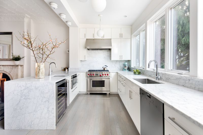 The open kitchen features white cabinetry, white marble countertops, and stainless steel appliances.