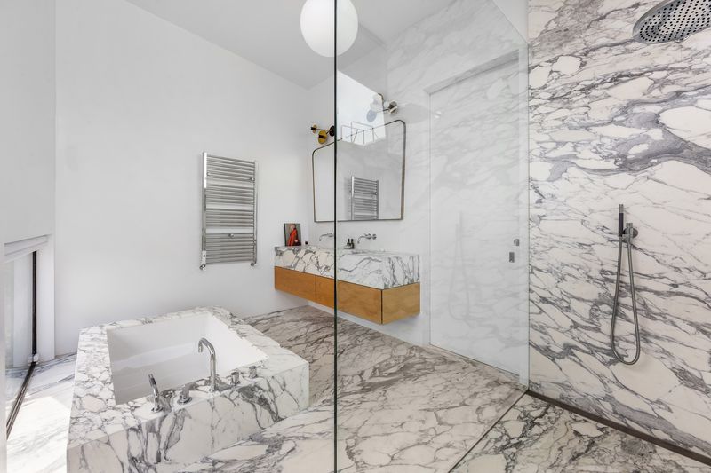 A bathroom with marble-covered walls, a deep tub, and a shower stall. 