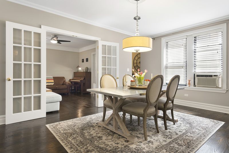 A dining area with hardwood floors, beige walls, crown moldings, a table with four chairs, and a rug.