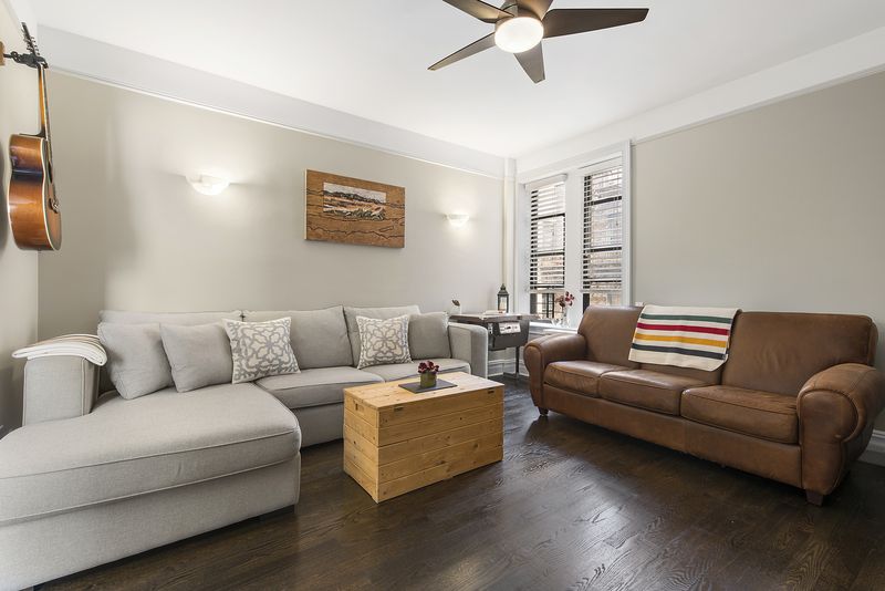 A living area with hardwood floors, beige walls, crown moldings, and a light grey couch.