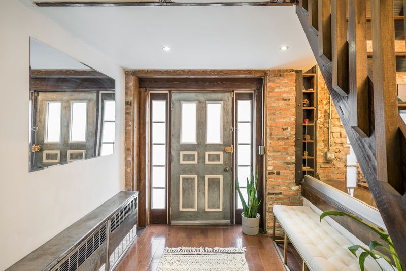 An entrance with exposed brick, hardwood floors, and a wooden staircase on the right side.