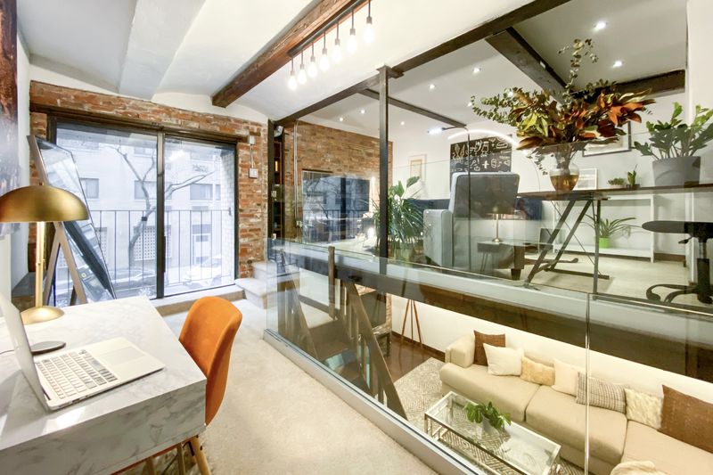 An office nook with exposed brick, a glass wall, and a Juliet balcony in the back. 