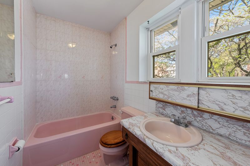 A bathroom with two windows and a pink bathtub.