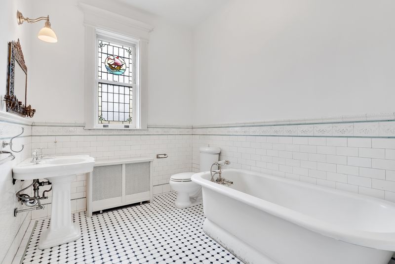 A bathroom with a small stained glass window and hexagon floor tiles. 