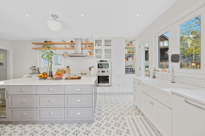 A kitchen with a large island, grey and white tiles, and white cabinetry.
