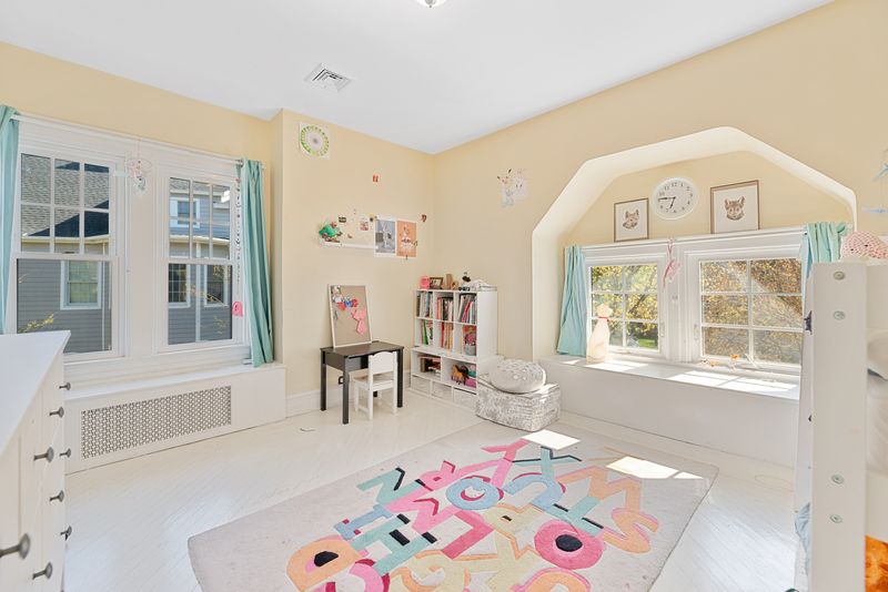 A children’s bedroom with light yellow walls, encased windows, and white furniture.