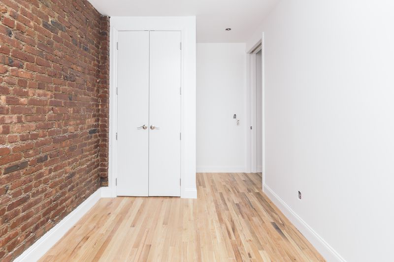 A bedroom with exposed brick, hardwood floors, a small closet, and white walls.
