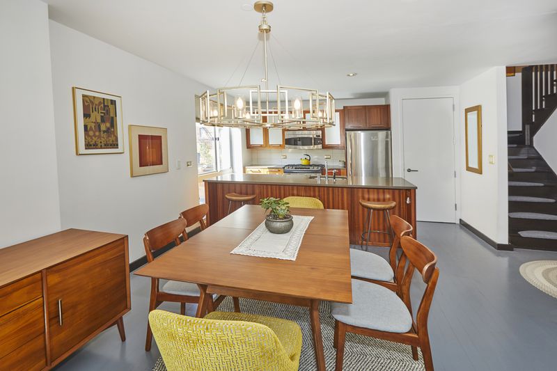 A living area with a chandelier, wooden furniture, a dining table, and a large kitchen island in the back.