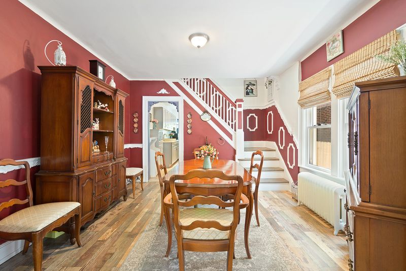 A living area with hardwood floors, two windows, wooden furniture, red walls, and a staircase in the back. 