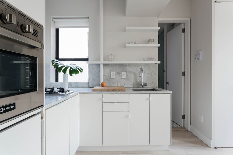 A kitchen with white cabinetry and a small window.