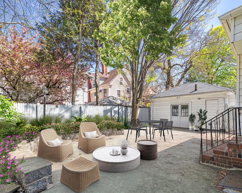 A backyard with a tree, several plantings, a wooden fence, and two seating areas. 
