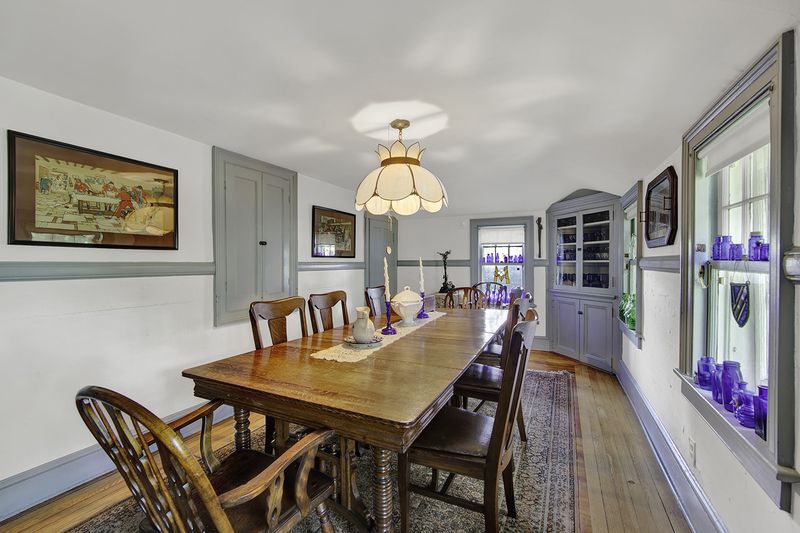 A dining area with a rectangular wooden table, hardwood floors, and base moldings.