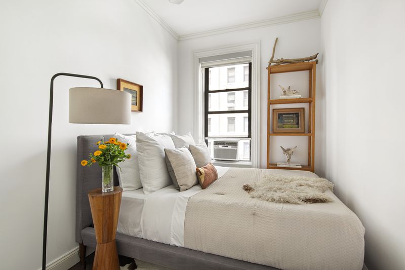 A small bedroom with a window, base moldings, and a queen-size bed.