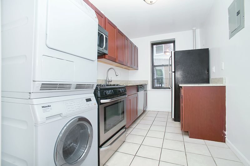 A kitchen with white walls, a small window, wood cabinetry, and in-unit washer/dryer.
