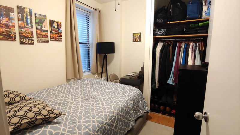 A bedroom with a small bed, a closet, a standing black lamp, and a small window.