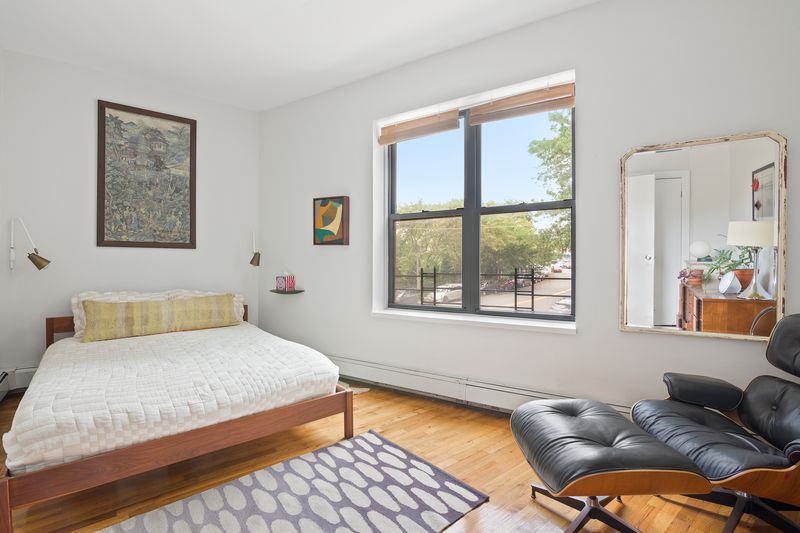 A bedroom with a large window, hardwood floors, a large bed, and a recliner leather couch.
