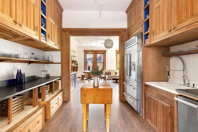 A kitchen with counters on both sides, stainless steel appliances, and a wooden table in the middle.