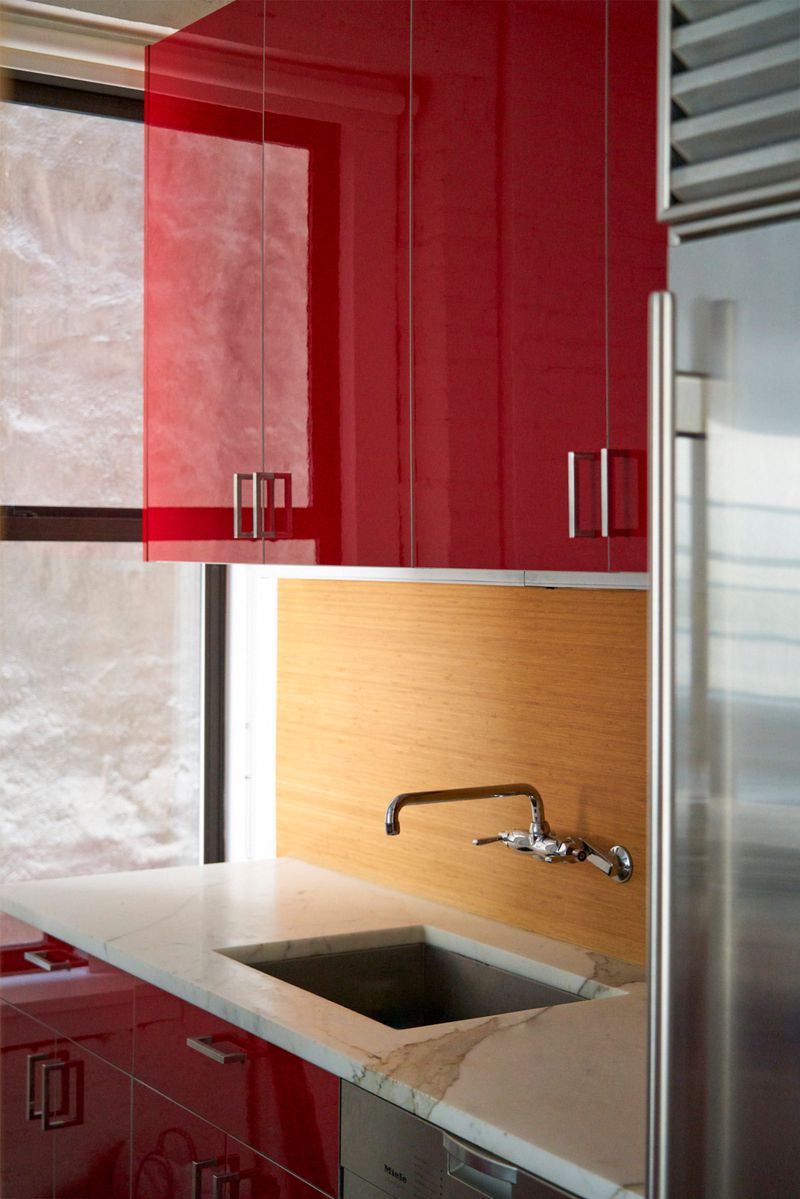 A close-up view of red kitchen cabinets, marble counters, and a stainless-steel fridge.