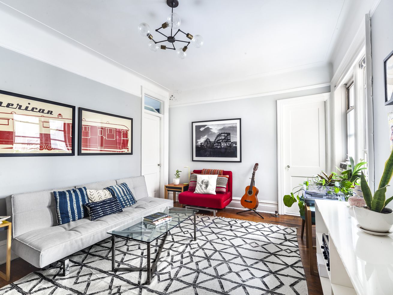A living area inside a Brooklyn Heights apartment with hardwood floors, a light grey couch, a glass coffee table, grey walls, and base moldings.